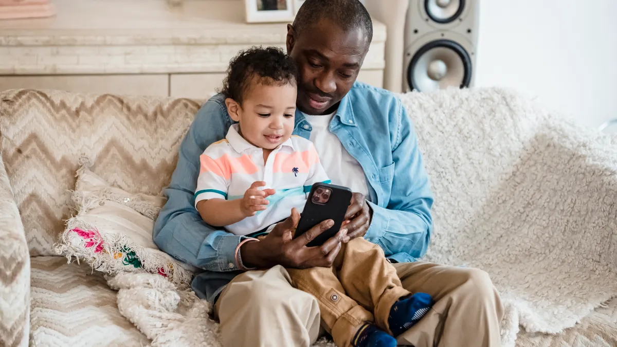 Man and toddler looking at a phone on a sofa